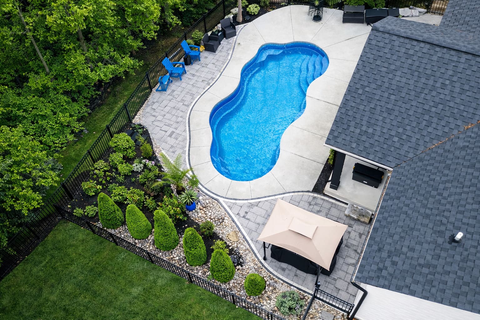 Aerial freeform pool with lush plantings and wooded lawn patio
