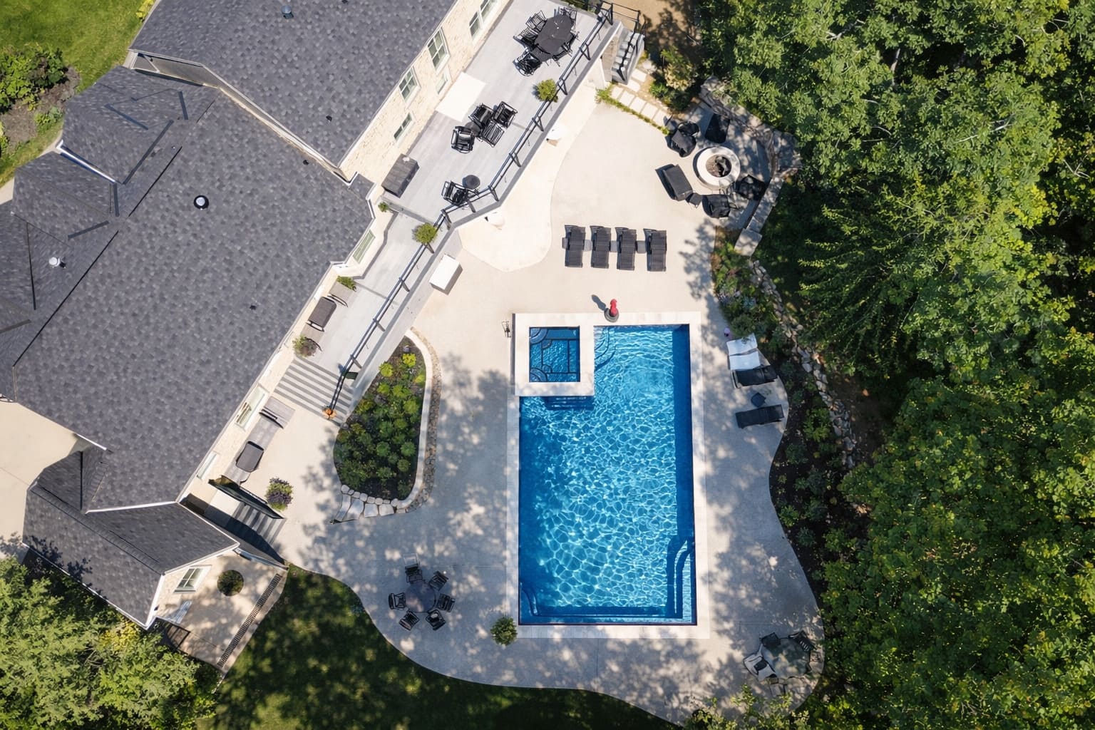 Aerial rectangular pool and spa with fire pit and wooded lawn