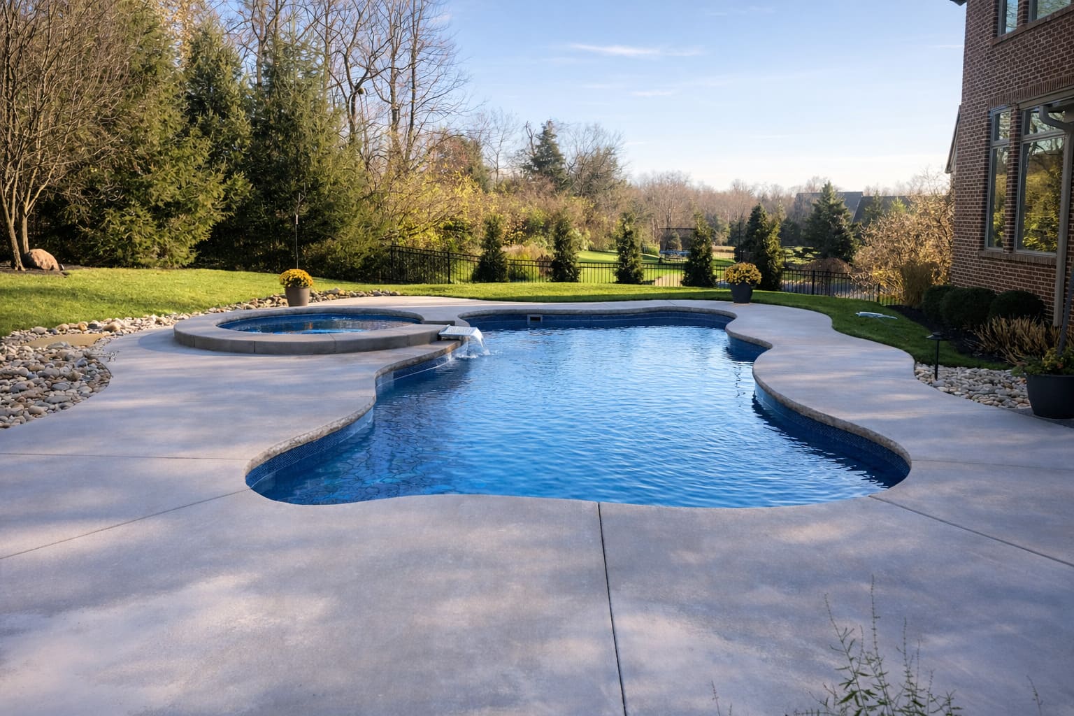 Freeform pool with circular spa waterfall and wooded lawn