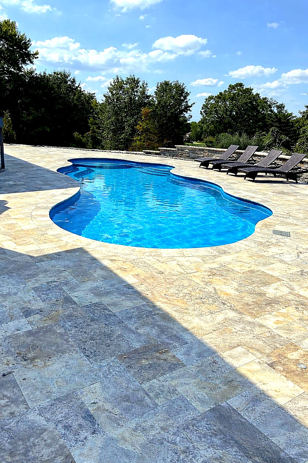 Freeform pool with travertine deck and lounge chairs