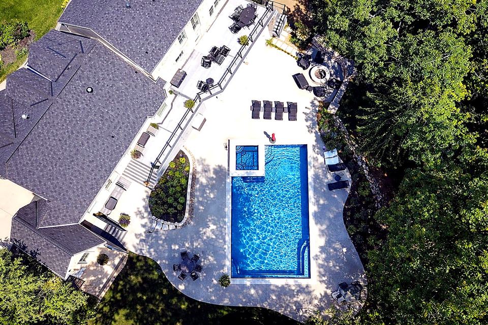 Large rectangular fiberglass pool and spa with a wide patio in a wooded backyard