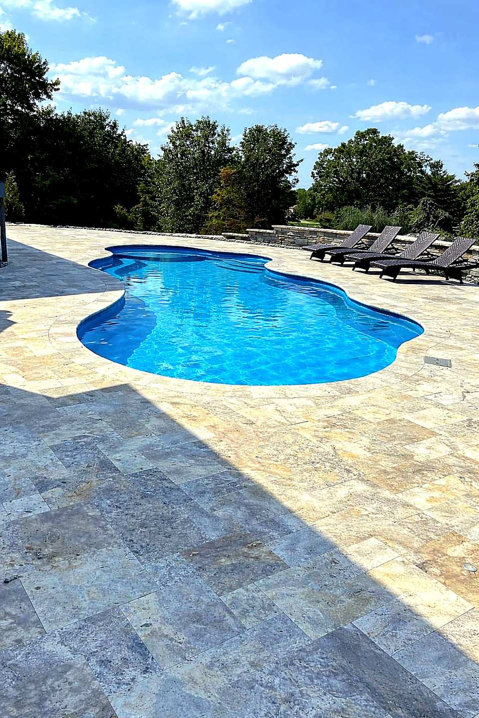 Freeform pool with travertine deck and lounge chairs