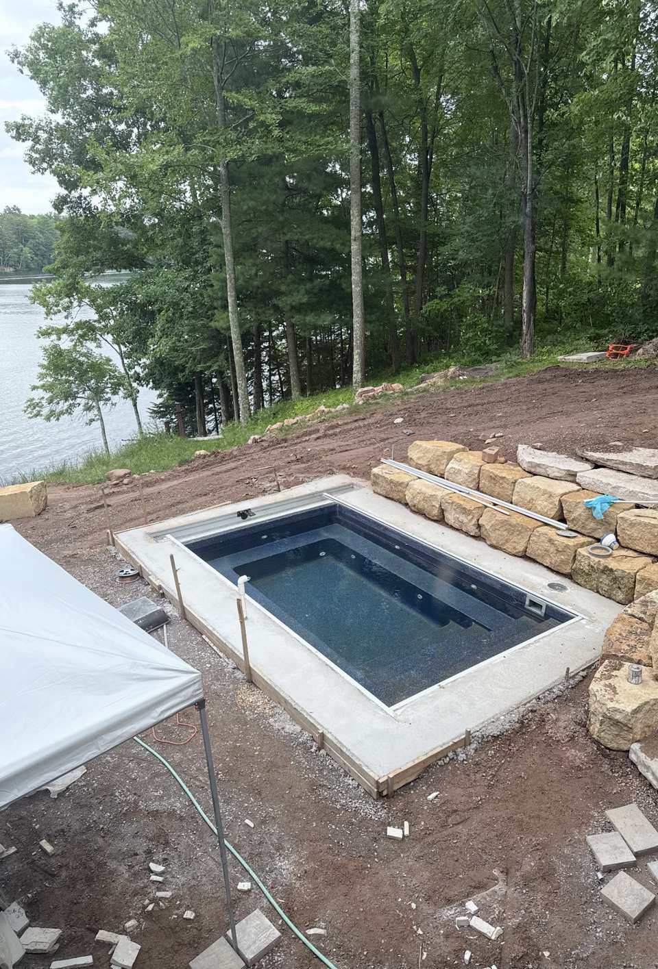 Fiberglass pool with concrete apron and cover tracks, lake visible through the trees, Long Lake WI