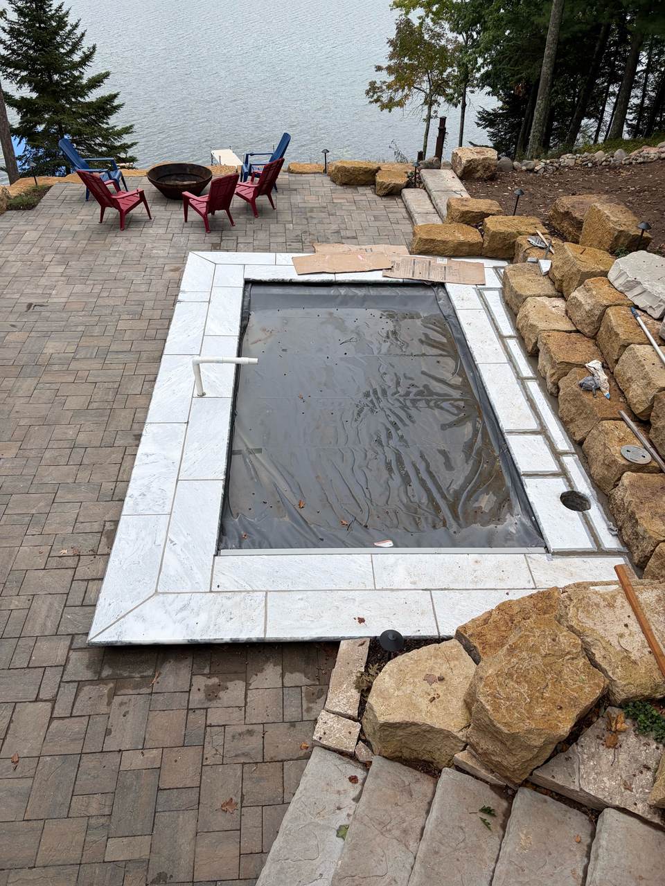 Stone coping and safety cover on the Long Lake fiberglass pool, paver patio running down to the lake
