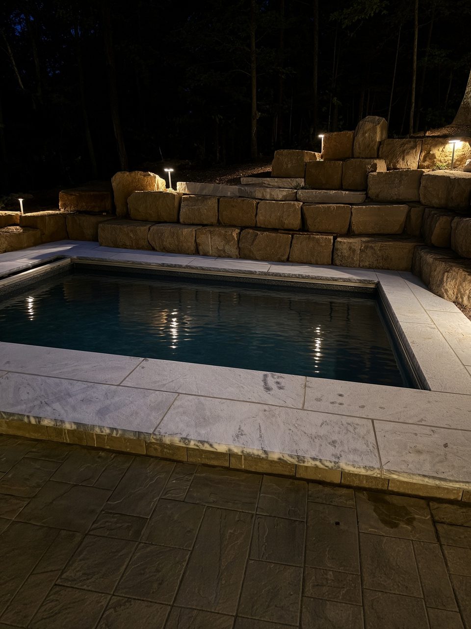 Long Lake, Wisconsin fiberglass pool lit up at night, limestone wall and coping